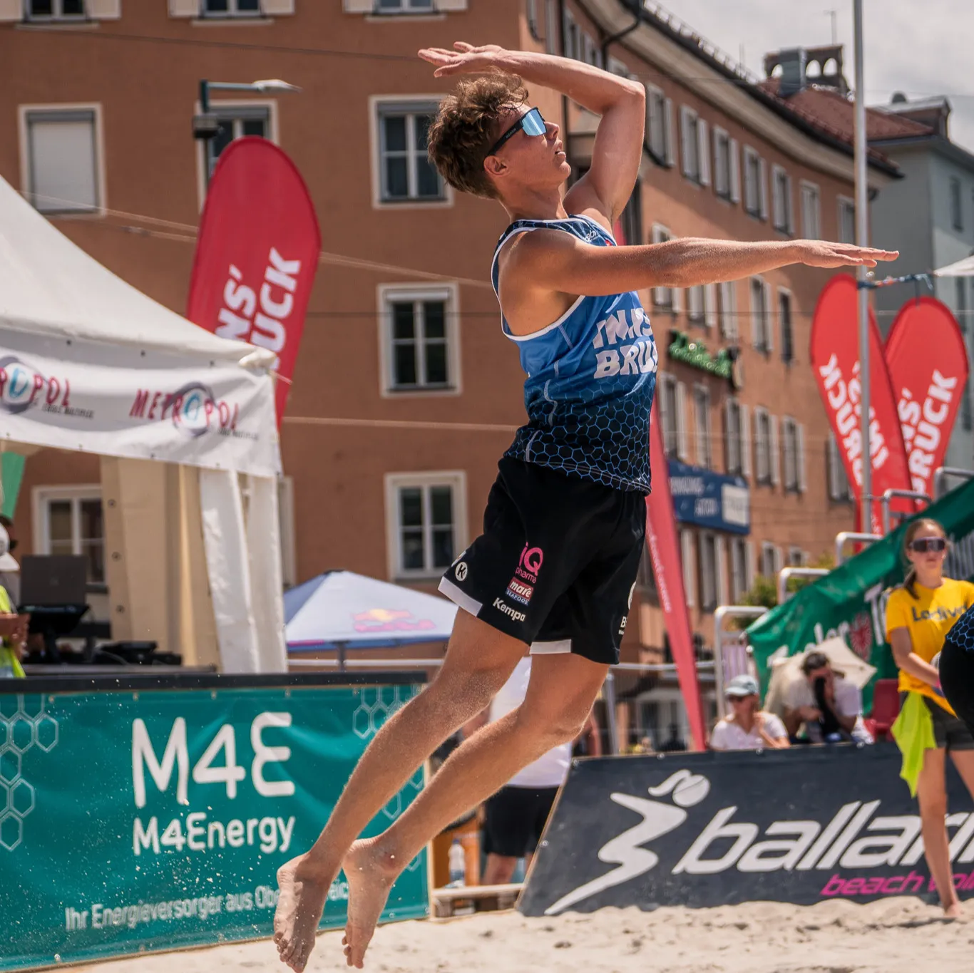 Beachvolleyball-Spieler im Sprung vor M4Energy-Bandenwerbung