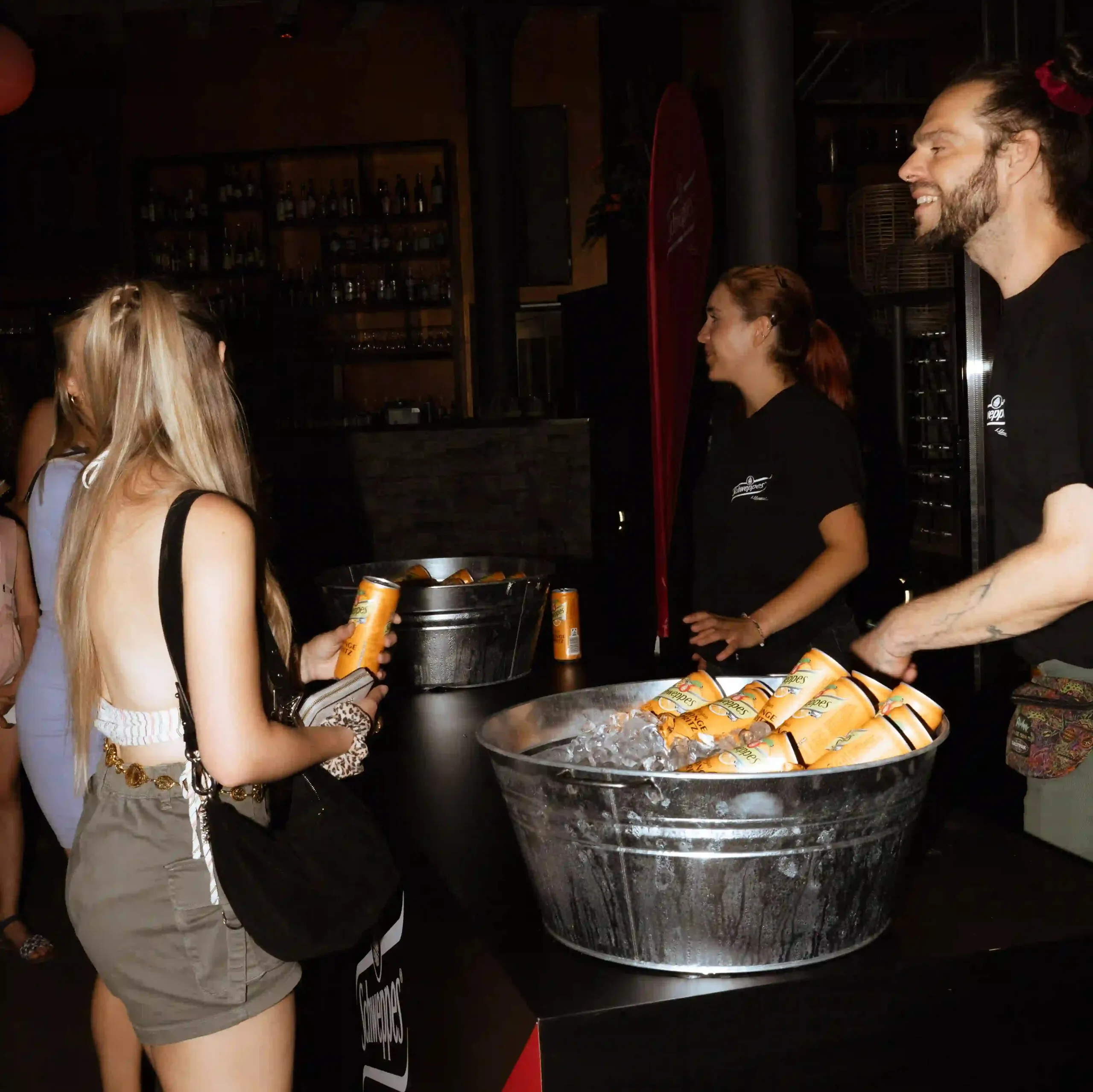 Schweppes-Promotion-Stand auf einem Event, Gäste nehmen gekühlte Dosen aus einer Metallwanne